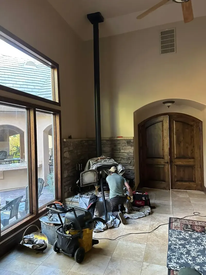 BH Chimney Sweep technician servicing a wood-burning stove and chimney flue inside a customer's home